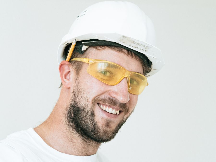 Smiling worker in a white hard hat and safety goggles looking at the camera